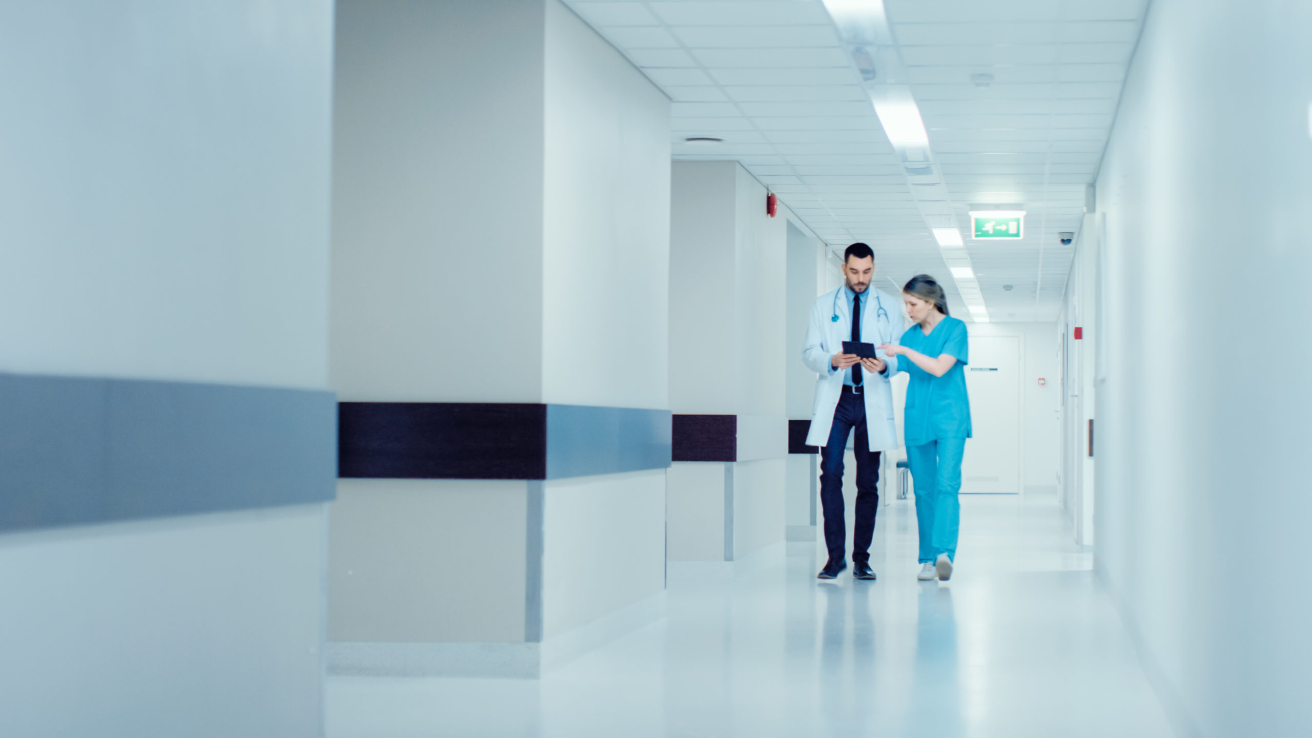 Surgeon And Female Doctor Walk Through Hospital Hallway They Consult